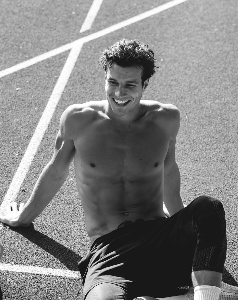 Coach is smiling and sitting on the floor topless.